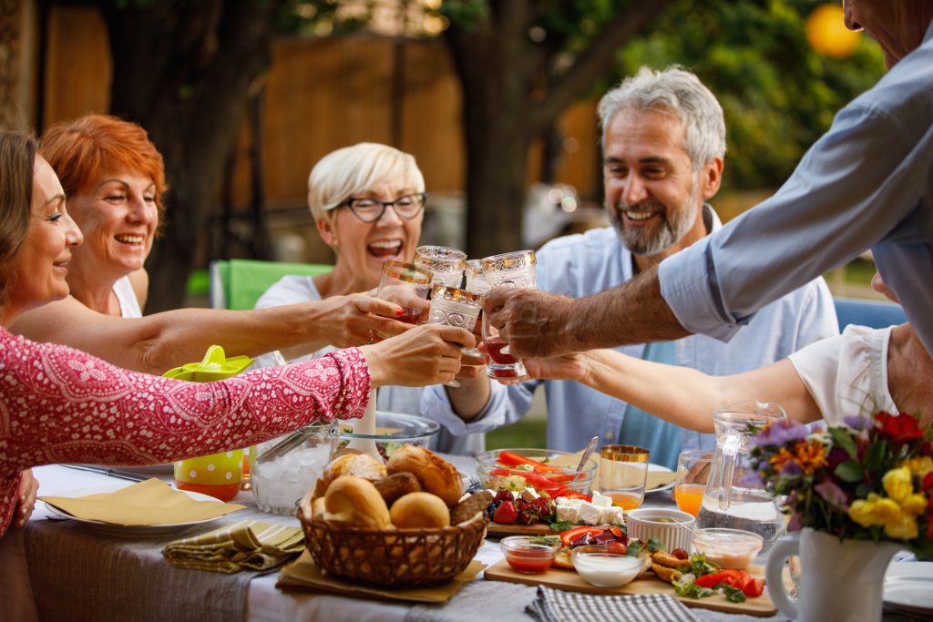 Group Of Joyful Senior Friends Cheering With Glasses Of Red Wine During Dinner Party