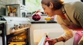 Mid Adult Woman Opening Oven To Check Cookies In Kitchen At Home