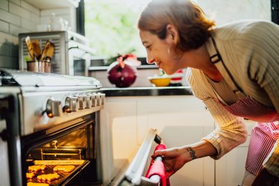 Mid Adult Woman Opening Oven To Check Cookies In Kitchen At Home