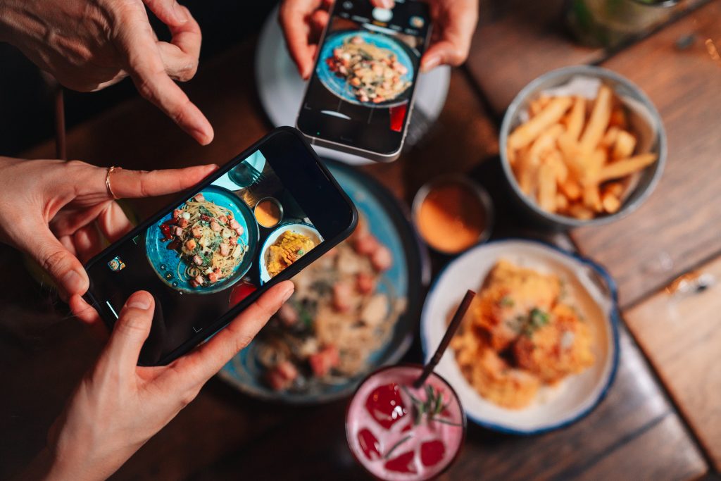 Close Up Shot Of Group Of Friends Using Their Smartphones To Take Pictures Of The Food On The Table